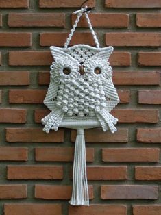 a crocheted owl hanging on the side of a brick wall with a tassel