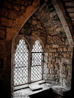 an old window in the middle of a stone building with a small bench underneath it