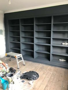 an empty room with many shelves and tools on the floor, while someone is painting it