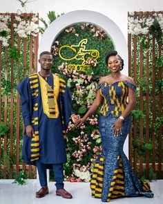 two people standing next to each other in front of a floral wall with flowers on it