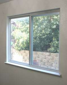 a window in the corner of a room with no curtains on it and trees outside