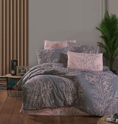 a bed with grey and pink comforters in a room next to a plant on the floor