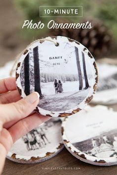 someone holding up an old photo ornament to show it on the table with pine cones in the background