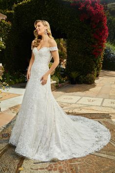 a woman in a white wedding dress standing on a floral garden path wearing an off - the - shoulder gown