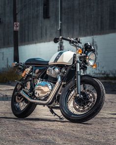 a white and black motorcycle parked in front of a building on a brick road next to a wall