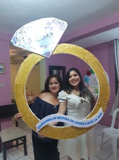 two women standing in front of a mirror holding up a gold ring with a diamond on it