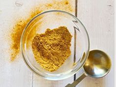 a glass bowl filled with spices on top of a wooden table next to a spoon