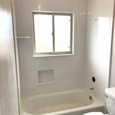 a white toilet sitting next to a bath tub under a window in a bathroom stall