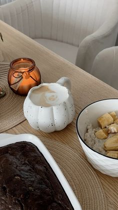 a table topped with bowls filled with food next to a bowl of pudding and a candle