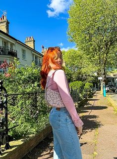 a woman with red hair is standing on the sidewalk in front of some houses and trees