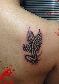 the back of a woman's shoulder with a heart and wings tattoo on it