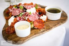 a wooden platter topped with lots of different types of food next to dipping sauces