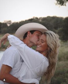 a man in a cowboy hat hugging a woman's face while she is wearing a white shirt and jeans