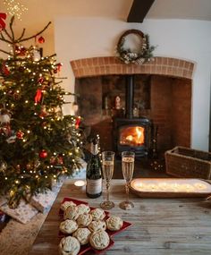 a christmas tree is next to a fireplace with cookies on the table and two champagne flutes