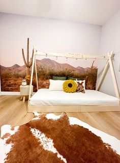 a bed with a brown and white cow skin rug in front of it, next to a desert wall mural