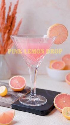 a pink lemon drop cocktail sitting on top of a table next to sliced oranges