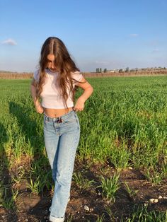 a woman standing in the middle of a field with her hands on her hips and looking down