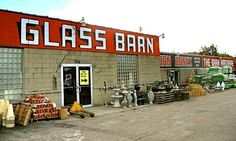 a glass barn with many items on the outside and large red sign that says glass barn