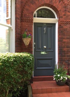 a blue front door with two potted plants on the steps and a brick building