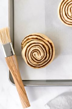 two cinnamon rolls sitting on top of a pan next to a brush