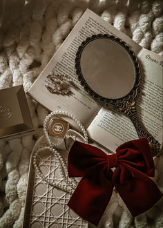 an open book with a red bow on top of it next to jewelry and a mirror