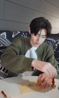 a young man sitting at a table cutting paper with scissors and glue on top of it