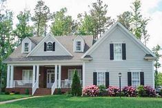 a white house with black shutters and flowers in the front yard