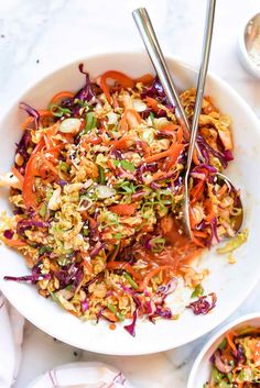 a white bowl filled with coleslaw slaw and two silver serving spoons