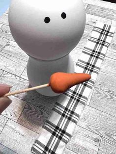 a person is holding a carrot in front of a small white object on a table