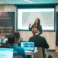 a woman is giving a presentation in front of a group of people sitting at desks