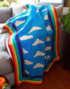 a crocheted blanket with clouds on it sitting on a couch next to a potted plant