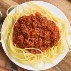 a white plate topped with spaghetti covered in meat and sauce on top of a wooden table