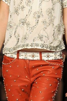 a close up of a person wearing red pants and a white shirt with silver beads on it