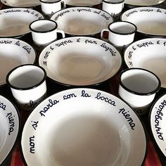 many white dishes with black rims and words written on the sides are lined up in rows