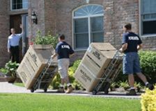 three men carrying boxes on their backs in front of a brick building with two windows