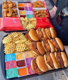 two trays filled with chicken sandwiches and waffle fries next to other food items