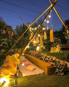 an outdoor party setup with balloons, lights and flowers on the grass in front of it