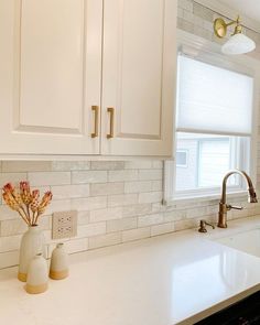 a white kitchen with marble counter tops and gold faucet lights above the sink