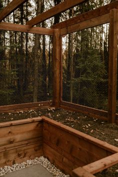 a chicken coop with rocks and gravel in the floor, surrounded by tall pine trees