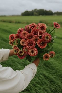 a person holding a bouquet of flowers in their hand on a field with green grass