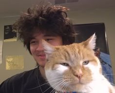 a man holding an orange and white cat in front of his face while he looks at the camera