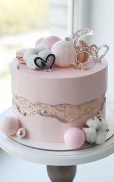 a pink and gold decorated cake sitting on top of a white table next to a window