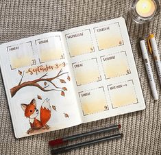 an open planner with a red fox on it next to some pens and pencils