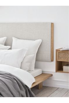 a bed with white linens and pillows on top of the headboard, next to a night stand