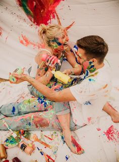 two people sitting on the ground covered in paint and confetti, with one person holding a baby