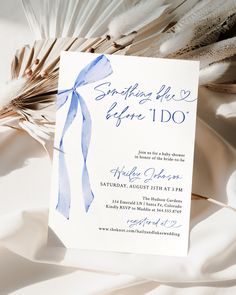 a white and blue wedding card with a ribbon on it sitting next to some feathers