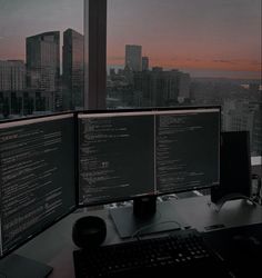 two computer monitors sitting on top of a desk in front of a cityscape