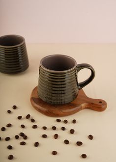 two coffee mugs sitting next to each other on a wooden board with coffee beans scattered around them