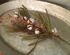 some cotton flowers are sitting on a silver plate with red berries and green stems in it