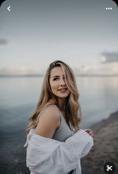 a woman standing by the water with her arms crossed and looking at the camera while wearing a white top